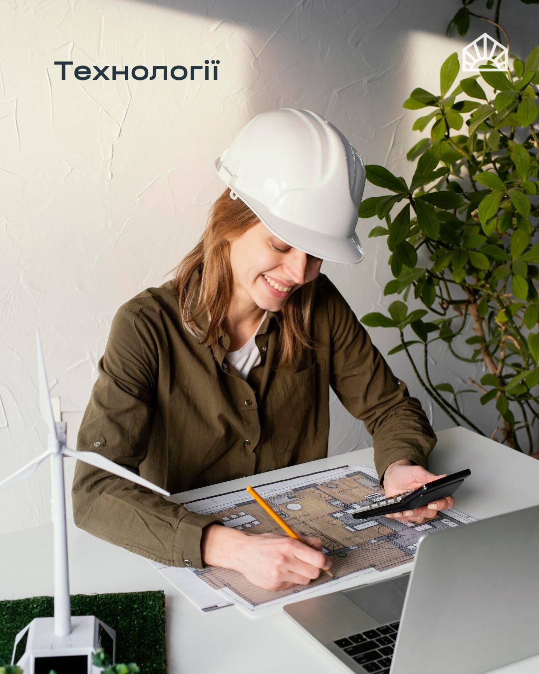 Woman in a white hard hat draws on architectural blueprints at a desk, with a laptop and greenery nearby.