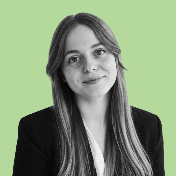 Portrait of a smiling woman with long hair in a black blazer against a pale green background.