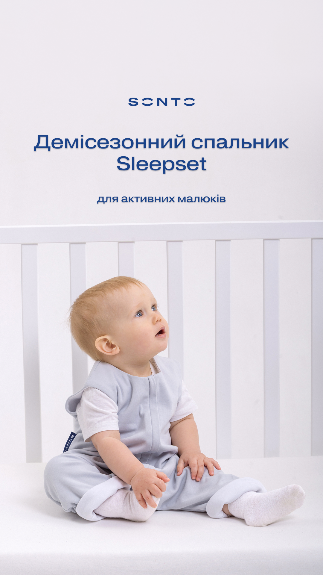 Baby sitting in a white crib wearing a light gray sleepsuit, looking up at a pale header with Ukrainian text: 'Демісезонний спальник Sleepset для активних малюків'