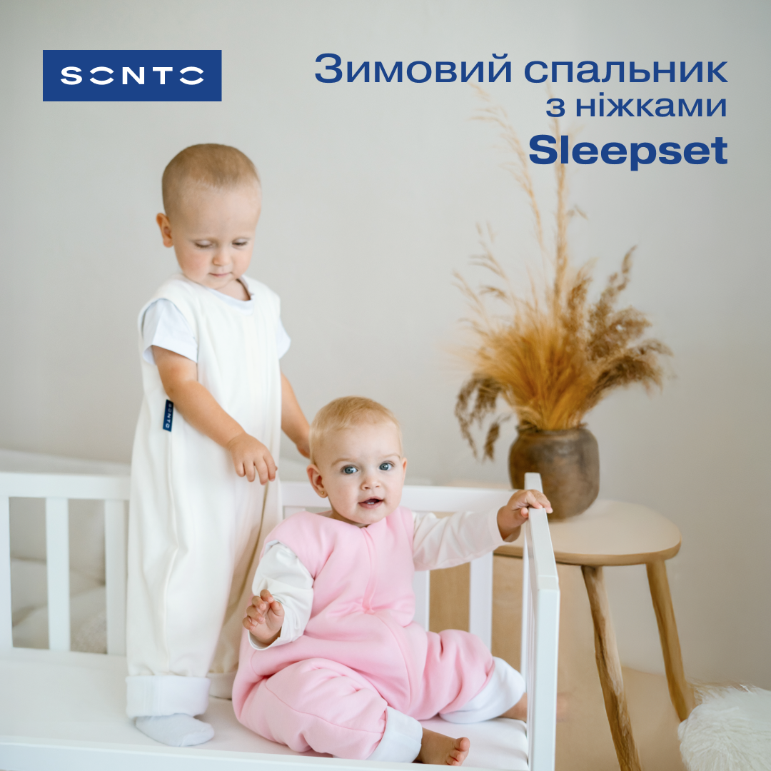 Two babies in a bright nursery: one stands in a white sleep sack, the other sits in a pink sleeper on a white crib, with a vase in the background and ad text in Ukrainian for Sleepset.