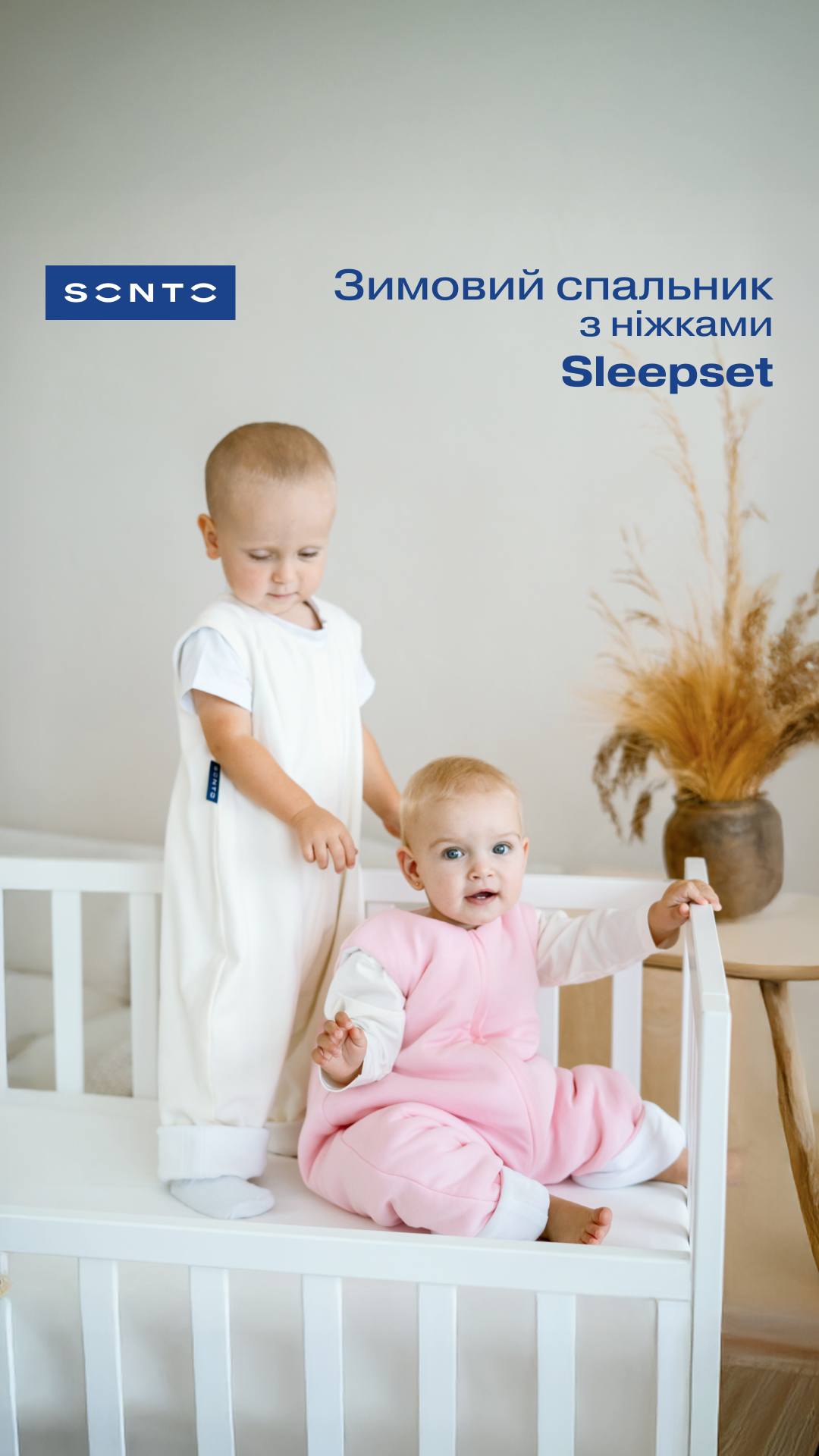 Two babies in a white crib indoors; one stands in white sleepsack while the other in pink sleepsuit sits, with a blue Sleepset logo and Ukrainian text in the background.