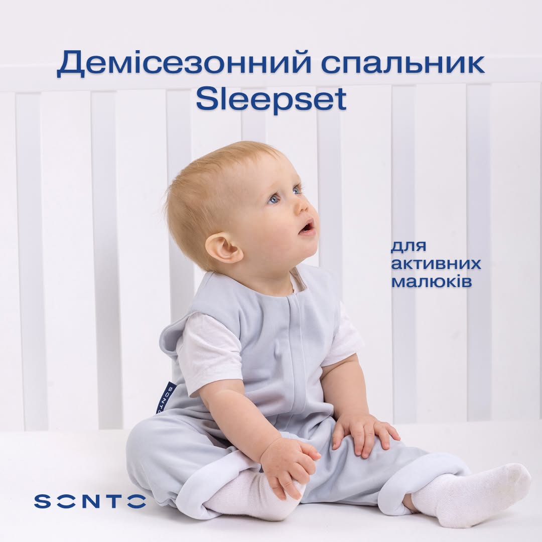 Young baby in a light gray sleepset sits on a white surface in a crib; Ukrainian ad text reads 'Demi-season sleep set' and 'for active little ones'.