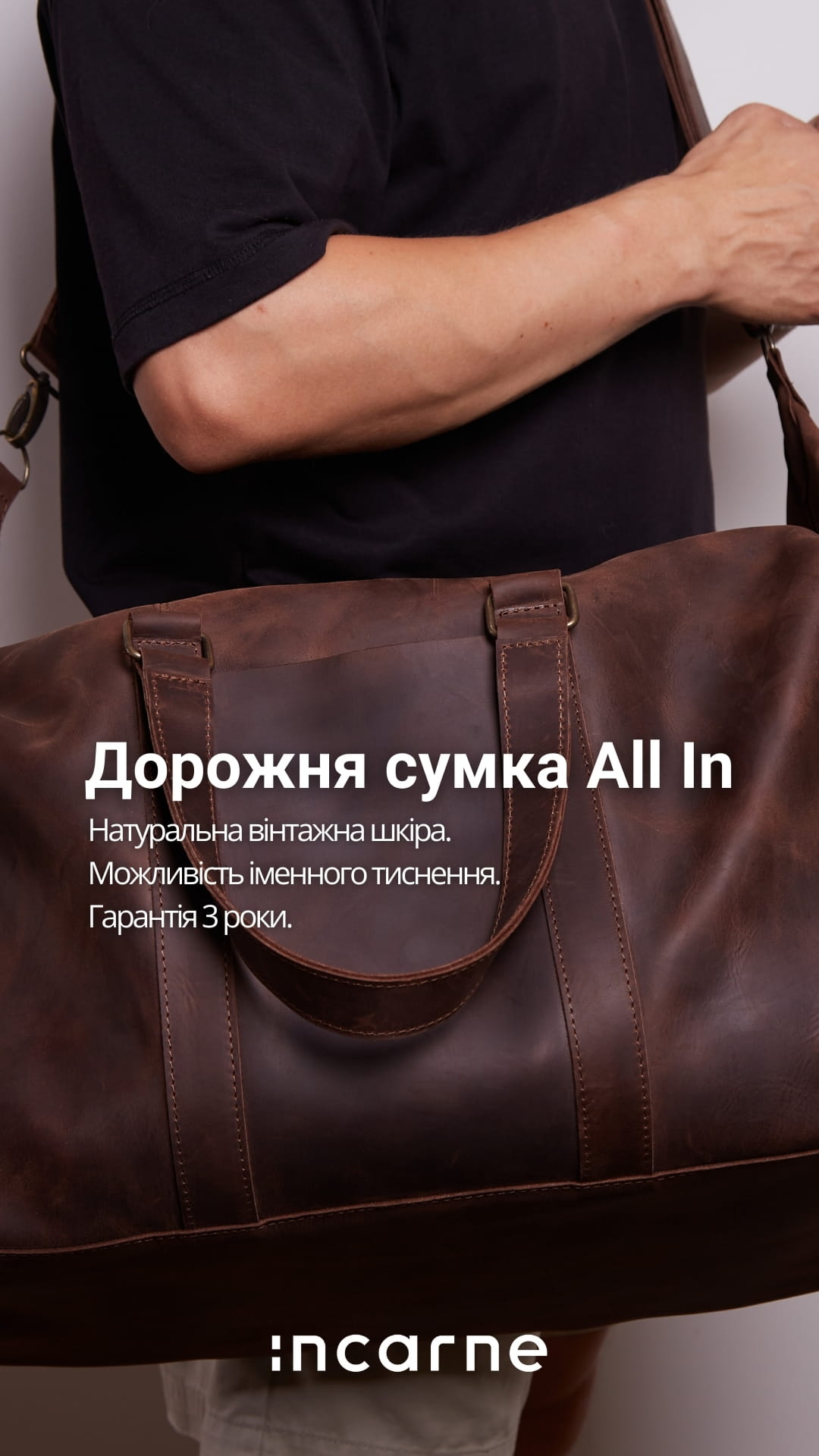 Крупним планом коричнева шкіряна дорожня сумка з ручками та плечовим ременем, на руці носія у чорній кофті