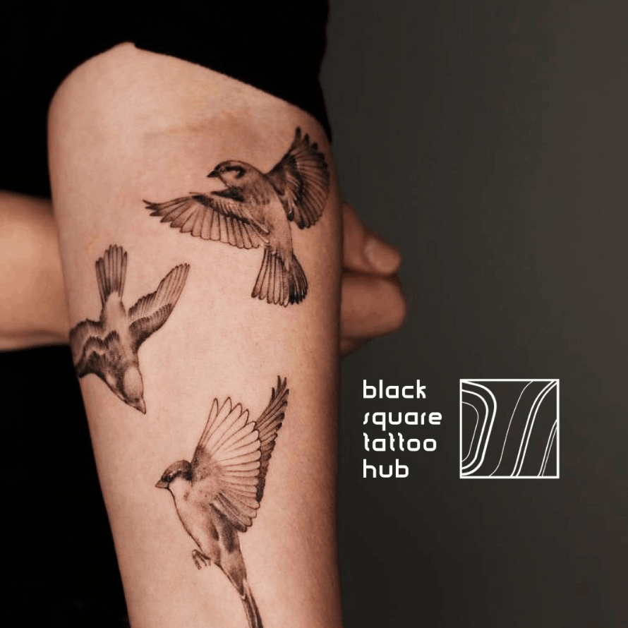 Forearm with three bird tattoos in flight, next to the Black Square Tattoo Hub logo and branding.